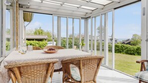 Une terrasse couverte avec une table et des chaises en osier, donnant sur un jardin et une maison.