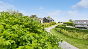Une maison moderne avec une allée pavée, entourée de jardins bien entretenus et sous un ciel dégagé.