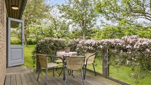 Une terrasse extérieure avec des chaises et une table en osier, entourée d’arbustes en fleurs et d’une clôture en bois.