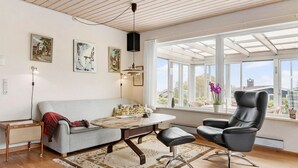 Un salon moderne avec un canapé, une table basse ronde, un fauteuil en cuir et une grande fenêtre donnant sur une maison et des arbres.