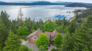 Un chalet à deux étages, entouré d’une forêt dense, qui offre une vue sur un lac paisible où sont amarrés des bateaux.