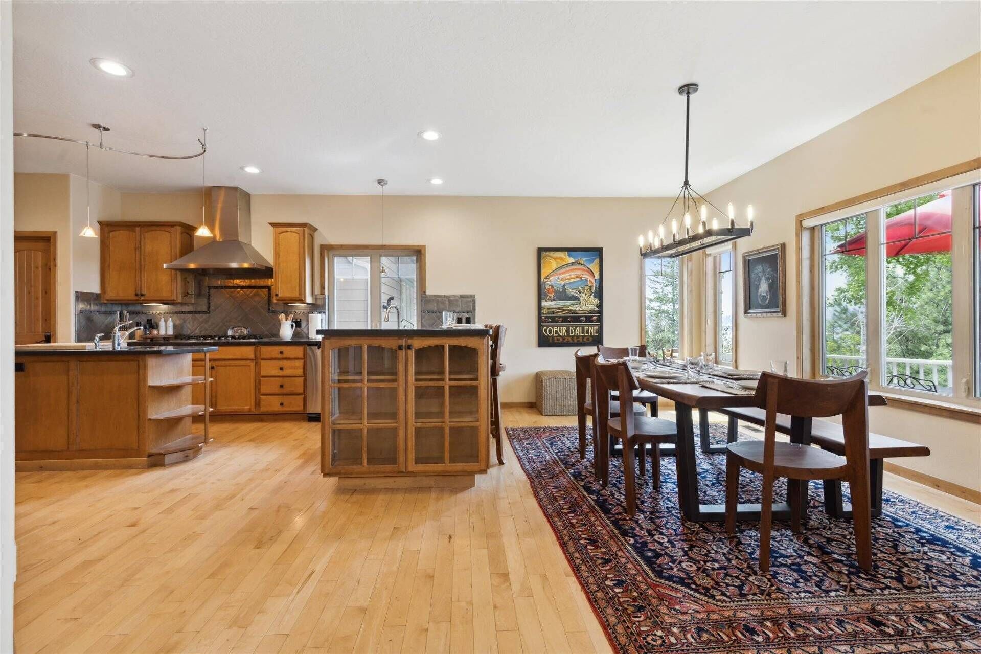 A spacious kitchen with wooden cabinets, a large island, and a dining area with a rug and chairs.