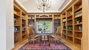 Une bibliothèque avec des étagères en bois, un lustre et une grande fenêtre.