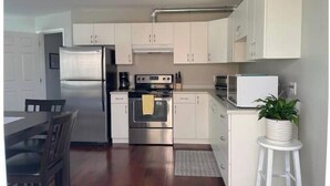 A modern kitchen with stainless steel appliances, white cabinetry, and a dining area with a wooden table and chairs. - Central Saanich cozy suite

 (Victoria)