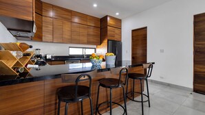 Une cuisine moderne avec des meubles en bois, un réfrigérateur noir, un panier de fruits et des tabourets de bar.