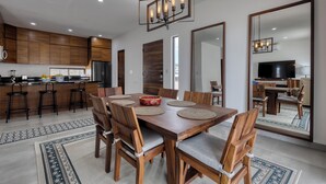 Une cuisine moderne avec des meubles en bois, un coin repas doté d’une grande table et de chaises, et un grand miroir qui reflète la pièce.