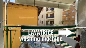 Een balkon met een tafel, een stoel en een wasmachine met de aanduiding 'LAVATRICE wasmachine'.