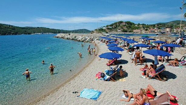 Een strand met helder water, mensen die zonnebaden en parasols.