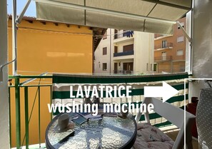 Ein Balkon mit Tisch, Stuhl und einer Waschmaschine mit dem Aufdruck 'LAVATRICE Waschmaschine'.