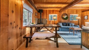 Un accogliente interno di una baita con un tavolo da pranzo in legno, panche, un divano blu e un camino.