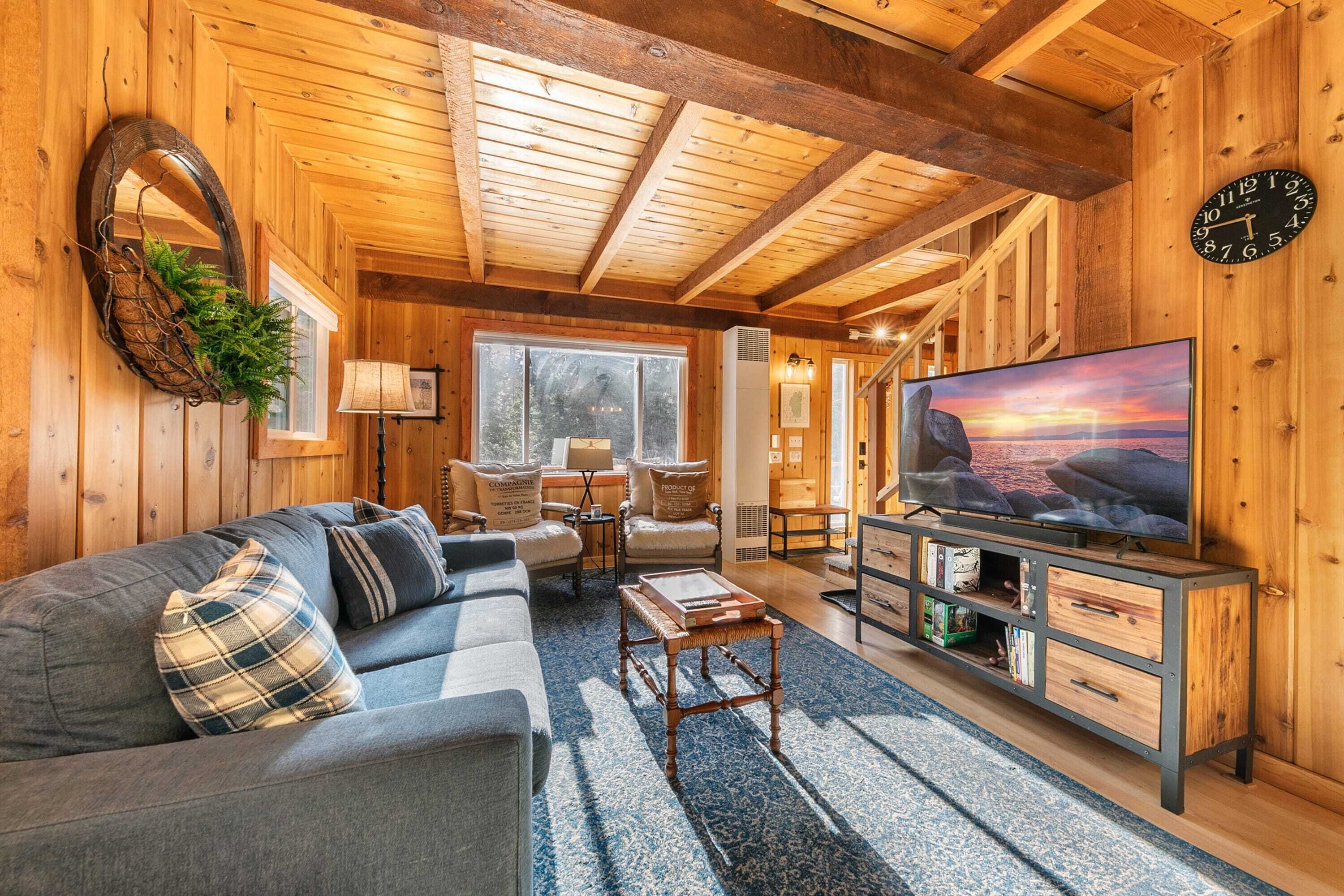 Ein gemütliches Blockhaushaus-Interieur mit Holzbalkendecke, einer Couch, einem Fernseher und einem Kamin.