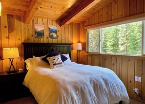 A wooden cabin room with a bed, two lamps, a window, and posters on the wall.