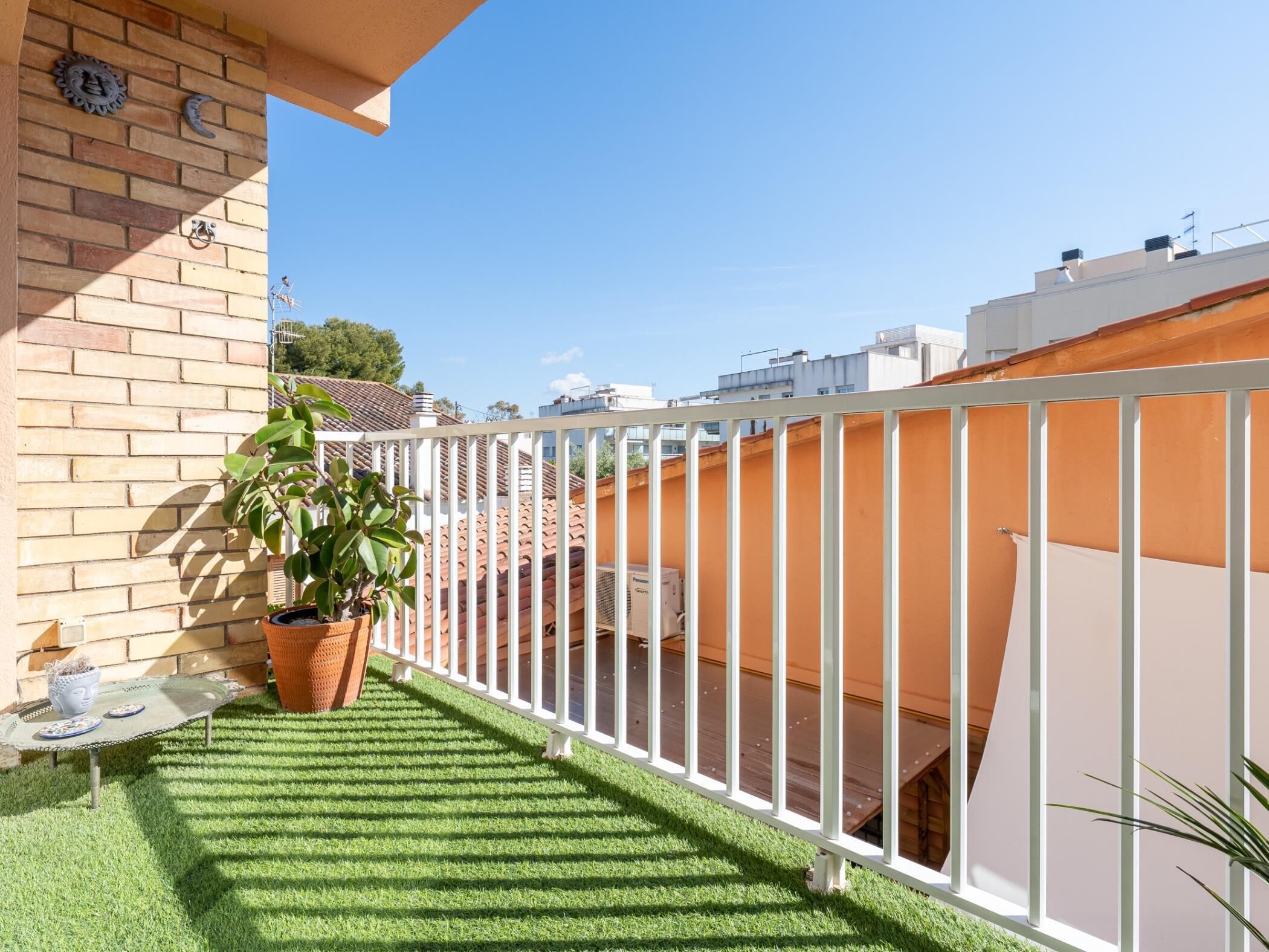 Un balcone con erba sintetica, una pianta in vaso e un corrimano bianco.