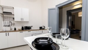 A modern kitchen with white cabinets, a black plate, wine glasses, and a coffee maker. - VivimiHome - [Navigli-Duomo] Maison Fusetti (Milano)