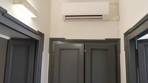 A hallway with dark wooden doors, a white air conditioning unit mounted on the wall, and a rectangular light fixture above the doors. - VivimiHome - [Navigli-Duomo] Maison Fusetti (Milano)