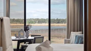 A hotel room with a large window, a bed, a table with a vase, and a view of a beach and water.