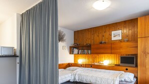 A bedroom with a bed, bedside lamps, a TV, a bookshelf, and a small desk with a computer.