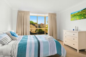 A bedroom with a large window, a bed with striped bedding, a dresser, and a painting on the wall.