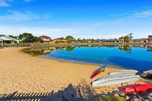 A beach with clear water, a sandy shore, and houses in the background.