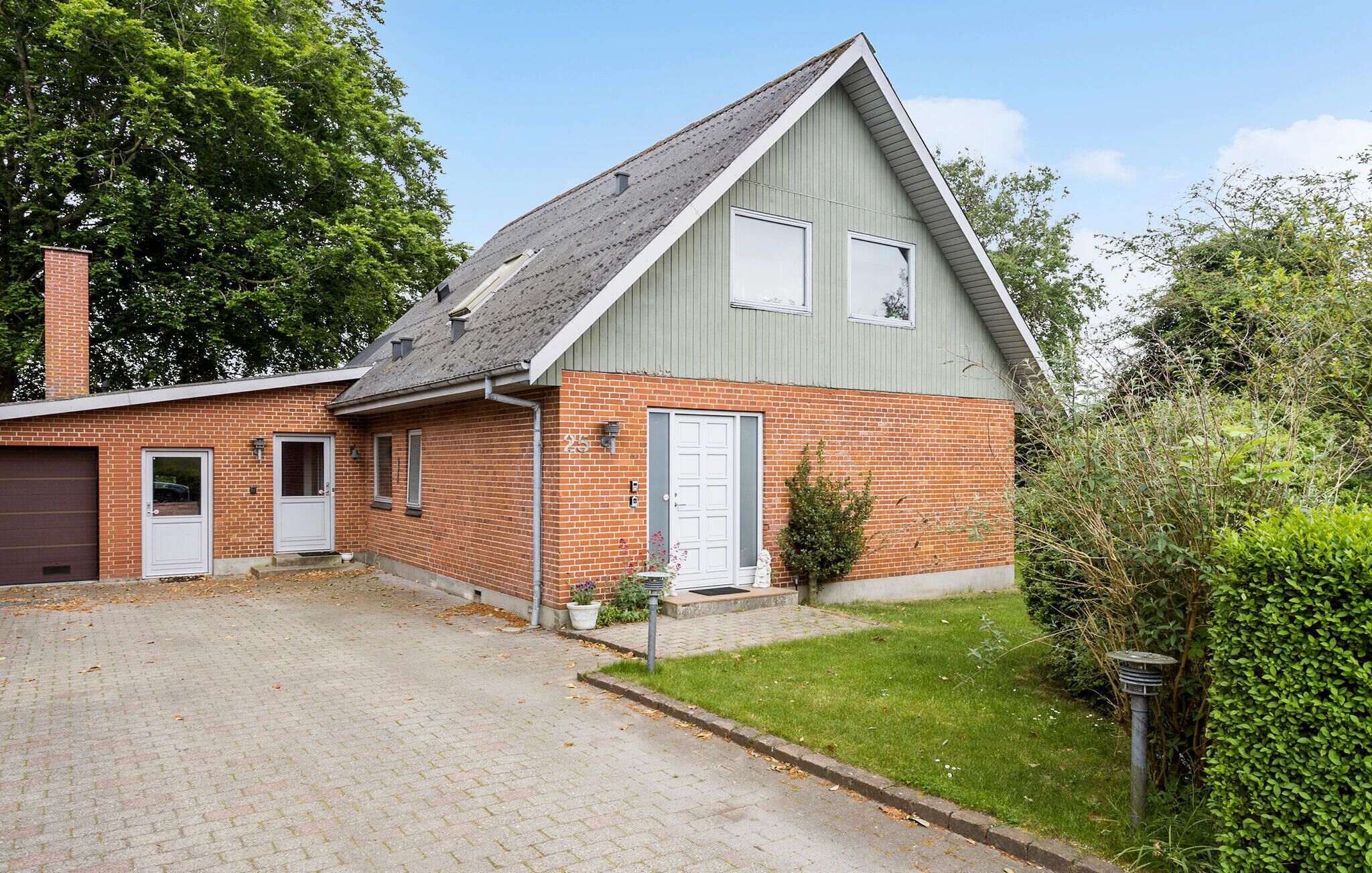 Ein zweigeschossiges Haus mit Backsteinfassade, grauem Dach und kleinem Vorgarten mit Hecke.