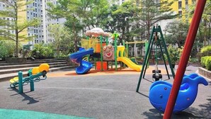 A playground with slides and swings, surrounded by trees and buildings. - Summarecon Springlake Basella  (Bekasi)