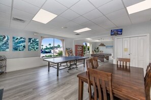 A spacious room with a ping pong table, wooden chairs, a television, and large windows with a view. - Condo# 411 Siesta Key Beach Sunsets (Sarasota)