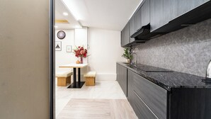 A modern kitchen with dark cabinetry, a wooden bench, and a vase with flowers. - Golden Suites 3 Apartments (Ho Chi Minh City)