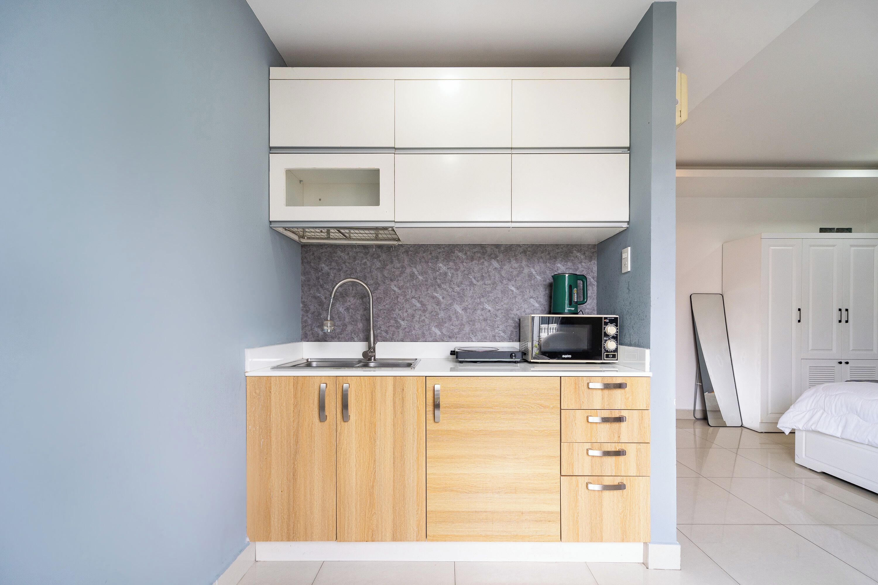 Una cucina compatta con mobili bianchi, un forno a microonde e un bollitore.