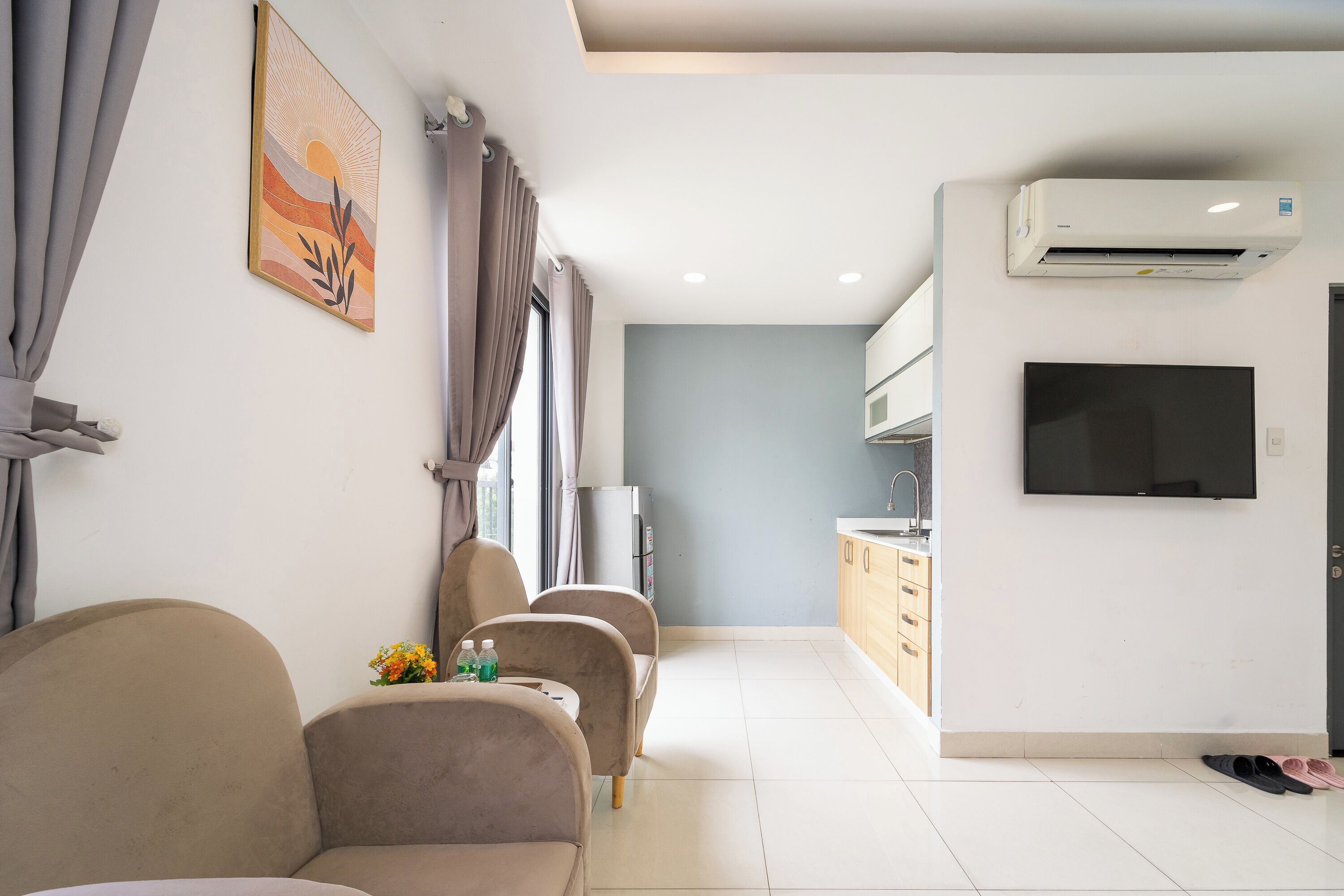 Una sala de estar moderna con un sofá, un televisor y una cocina al fondo.