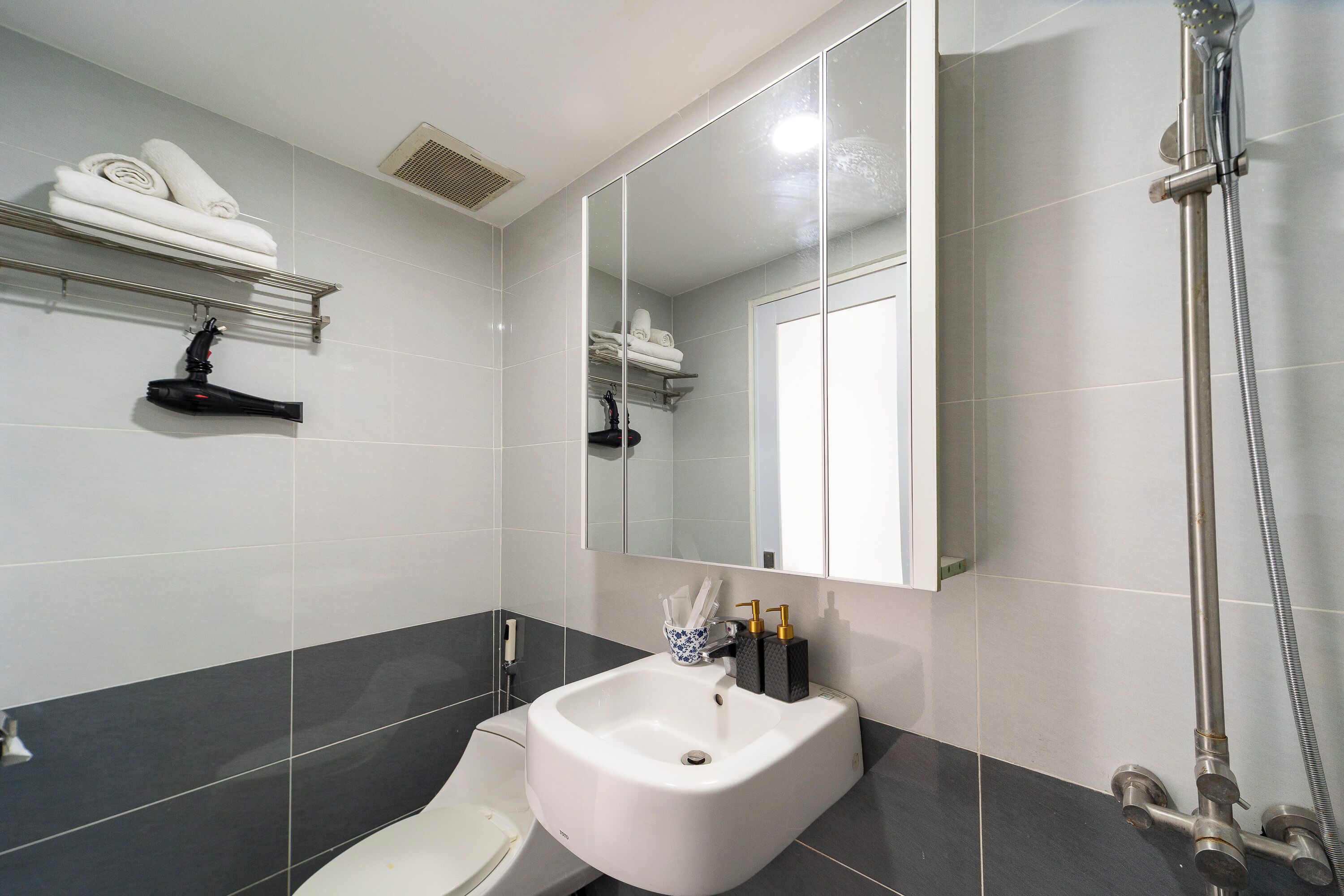 A modern bathroom with a white sink, dark tiled walls, a large mirror, and a shower area.