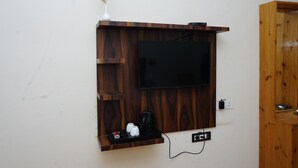 Un televisor de pared con estantes de madera abajo, un enchufe y una cafetera pequeña.