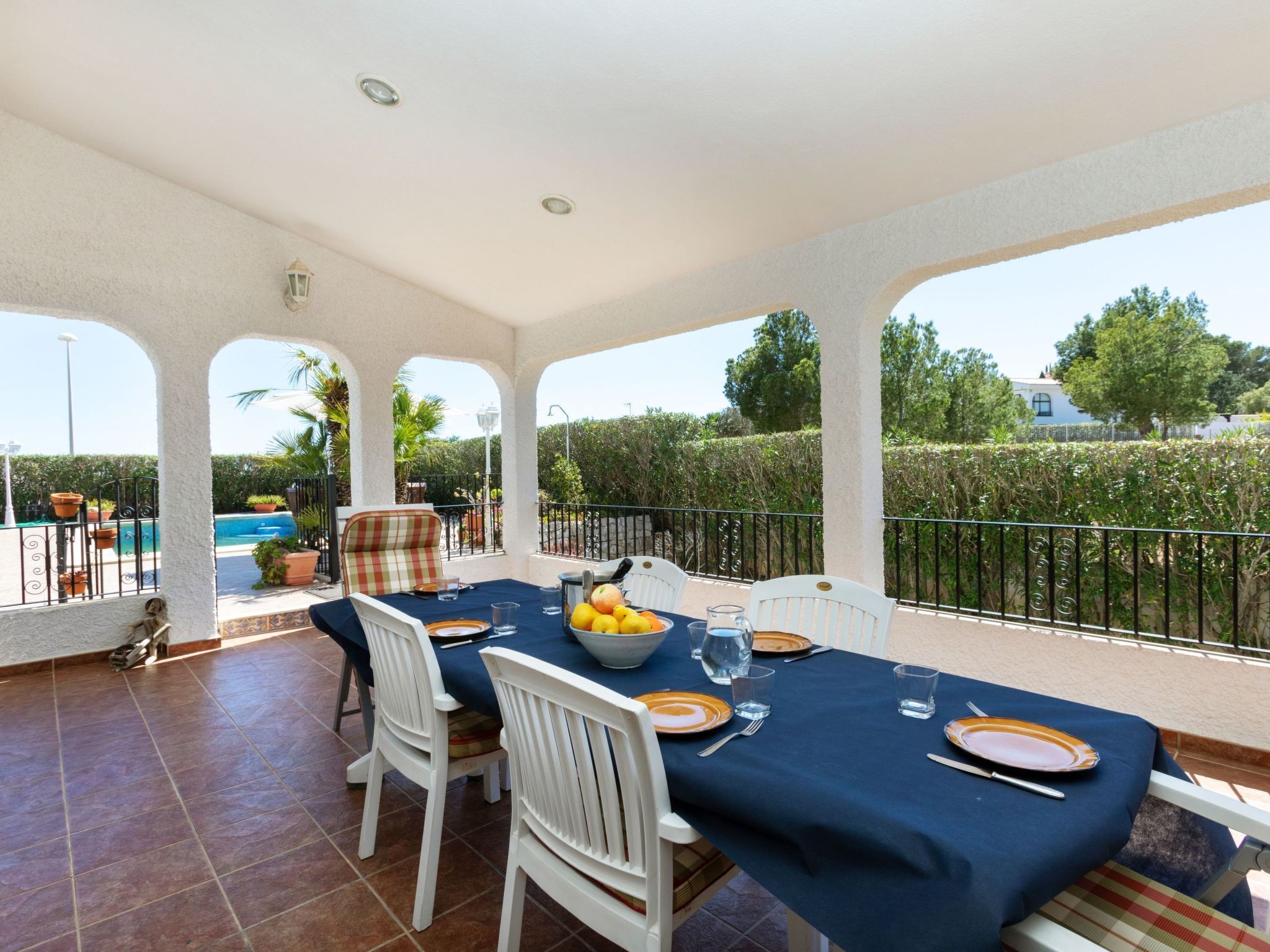 A covered outdoor dining area with a pool in the background.