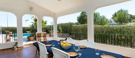 A covered outdoor dining area with a pool in the background.