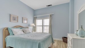 A bedroom with a bed, a window with curtains, a dresser, and a mirror. - OCHG OF Villas (Ocean City)