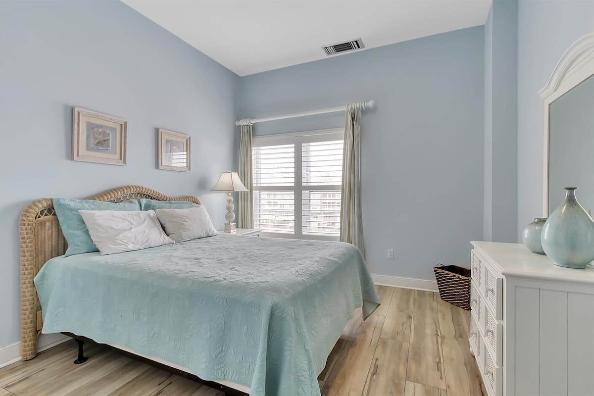 A bedroom with a bed, a window with curtains, a dresser, and a mirror.
