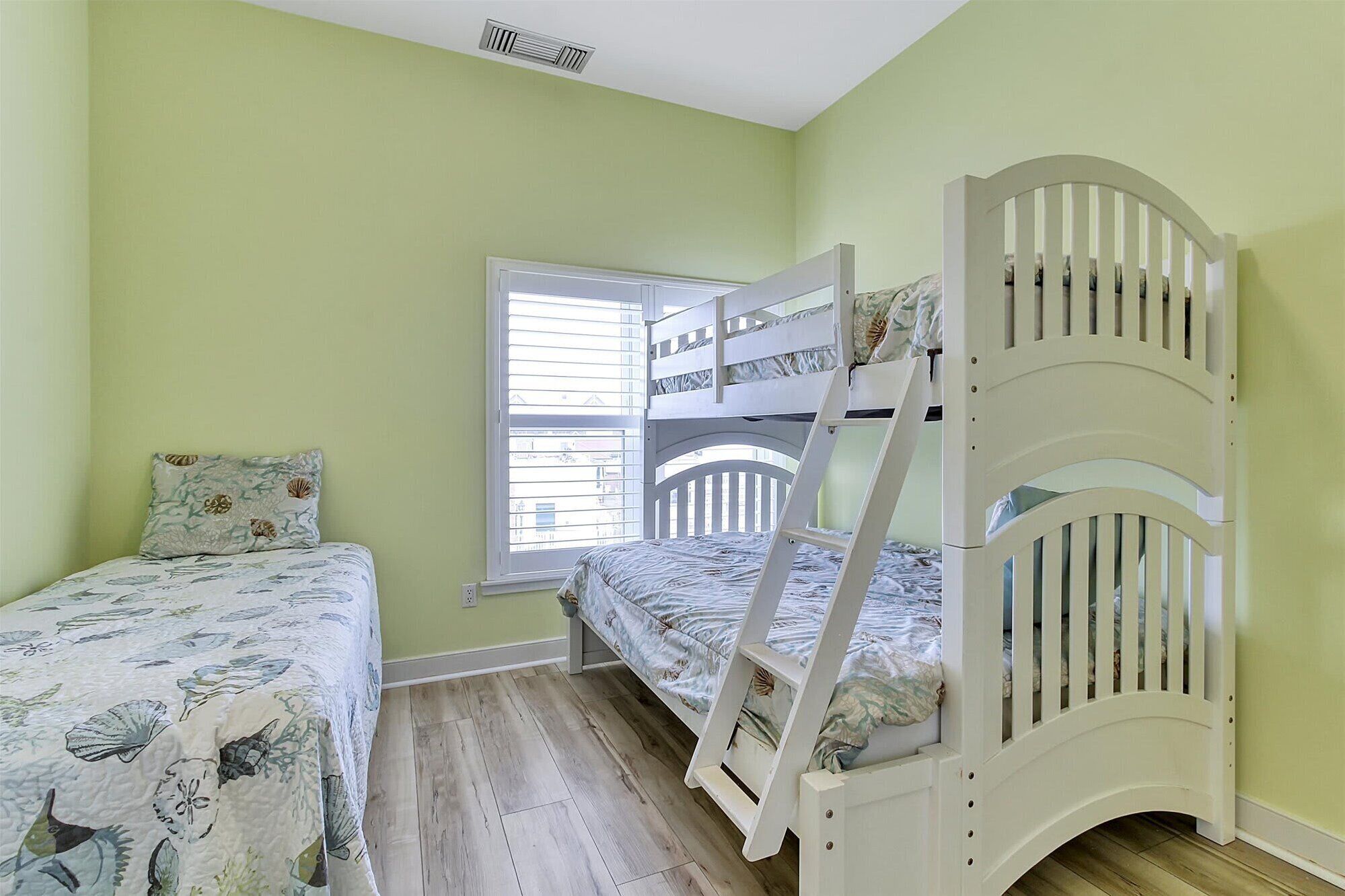 Habitación infantil con literas, una cama individual y un ventanal con persianas.