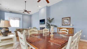 A dining room with a wooden table and white chairs, a ceiling fan, and a fireplace. - OCHG OF Villas (Ocean City)