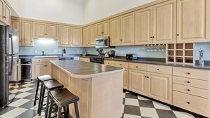A modern kitchen with light wooden cabinets, a central island with stools, a microwave, stove, and a sink. - OCHG OF Villas (Ocean City)