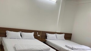 Habitació d'hotel amb dos llits de fusta, roba de llit blanca i una làmpada al sostre.