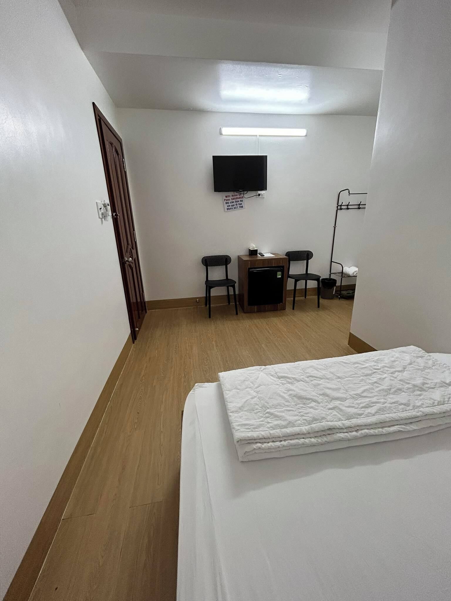 A hotel room with a bed, a desk with a chair, a television mounted on the wall, and a coat rack.