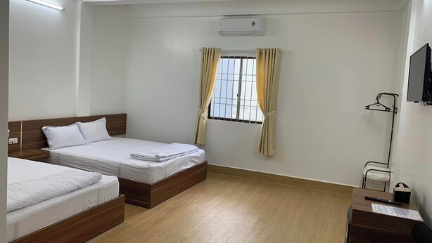 Habitació d'hotel amb dos llits individuals, un escriptori amb cadira, un televisor fixat a la paret i una finestra amb cortines.