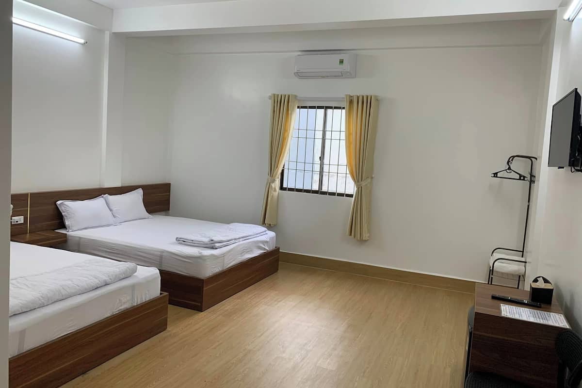 A hotel room with two single beds, a desk with a chair, a TV mounted on the wall, and a window with curtains.
