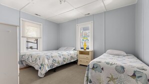 Un dormitorio con dos camas, una ventana con persianas, una lámpara en una mesita de noche y un ventilador de techo.