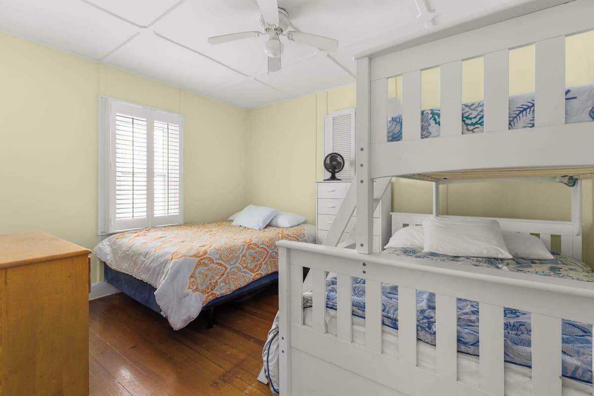 Une chambre avec deux lits, un ventilateur de plafond, une fenêtre avec des stores et une commode.