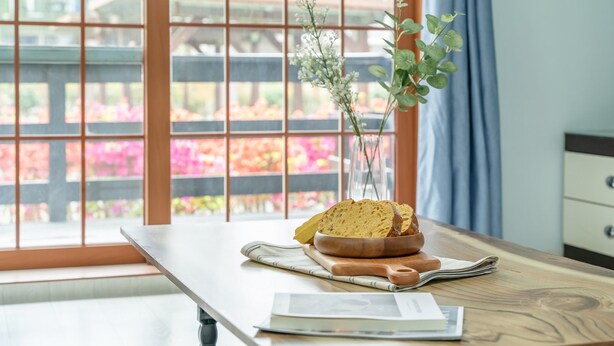 Une table en bois sur laquelle se trouvent un panier de pain, un livre et un vase rempli de fleurs.