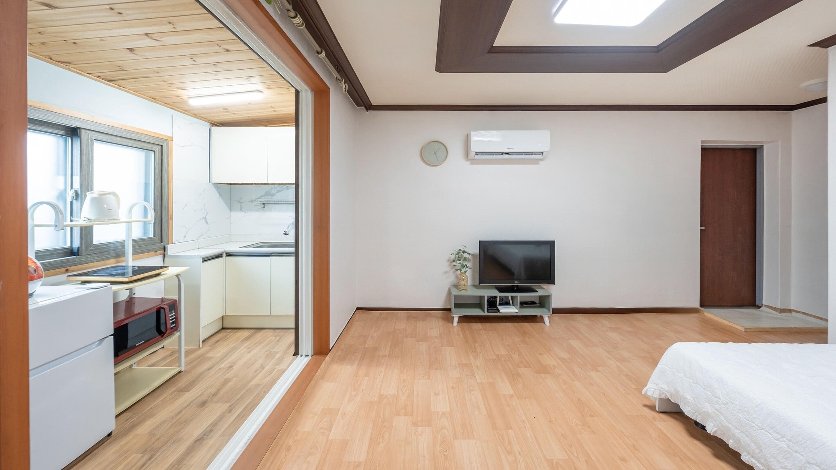 A modern, well-lit room with a kitchenette, a flat-screen TV, and a bed.