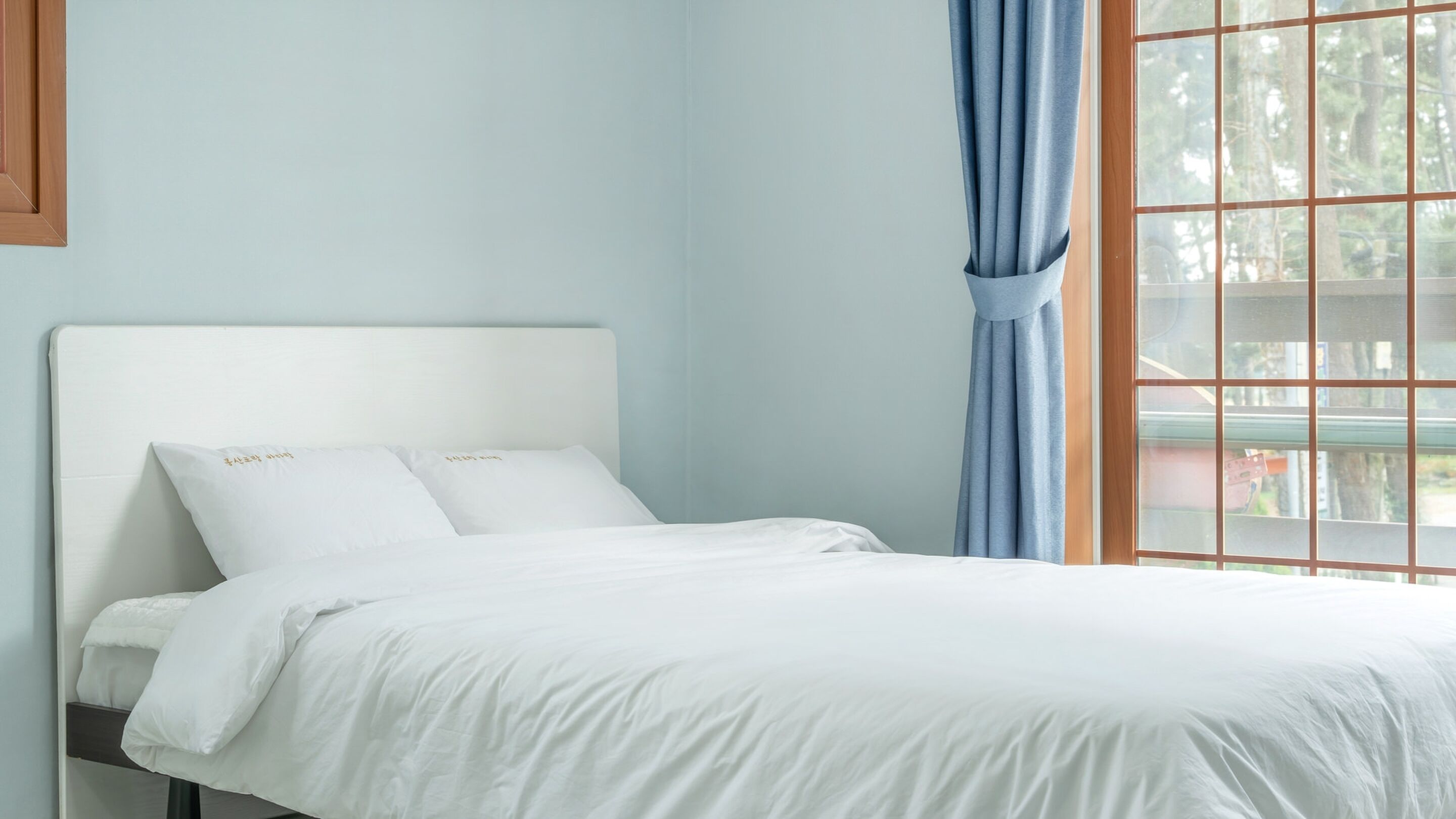 A bed with white bedding, a headboard, and two pillows with embroidered text.