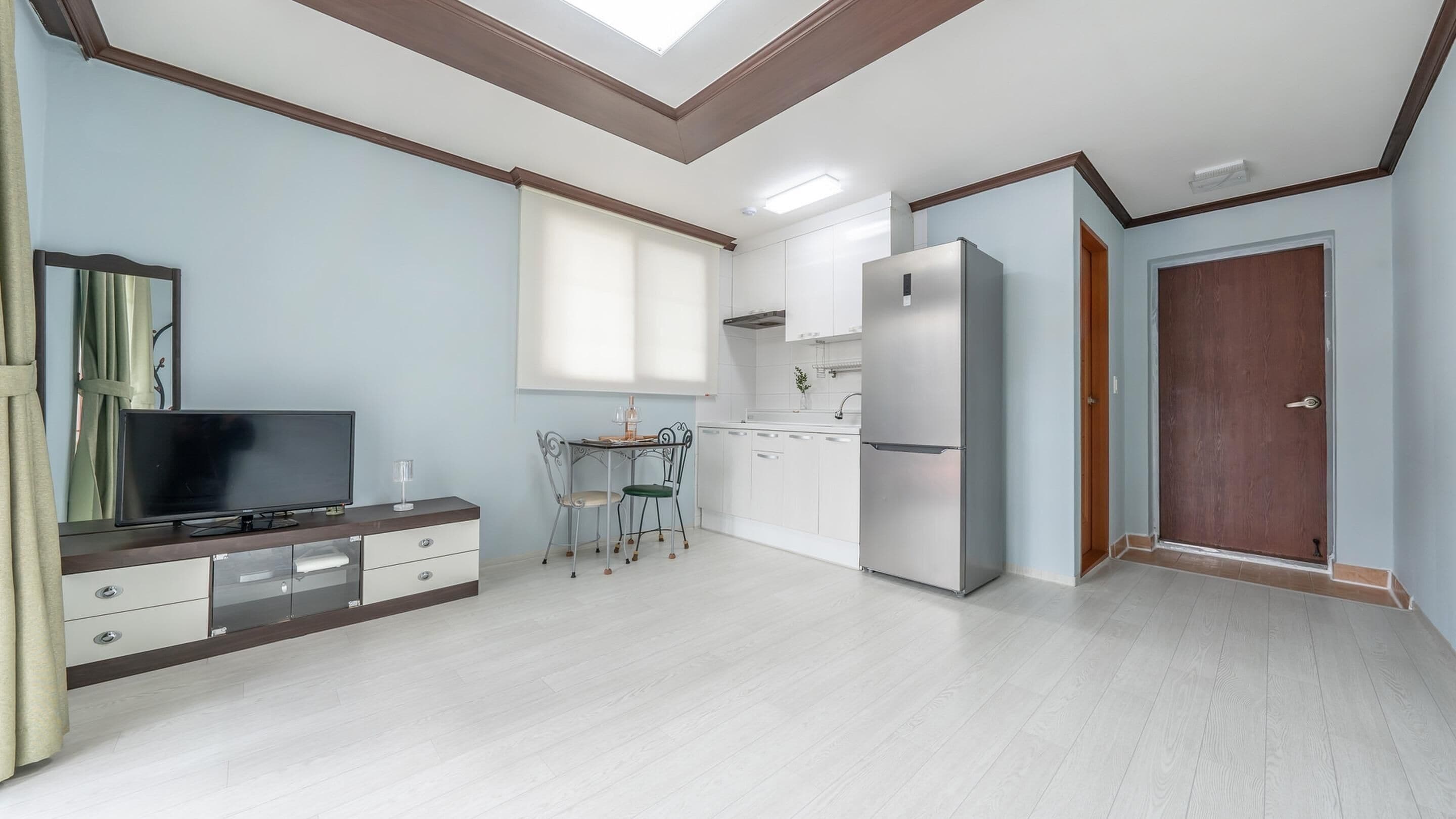 A modern kitchen with white cabinets, a stainless steel refrigerator, and a dining area with a table and chairs.