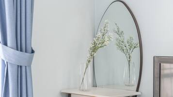 Un espejo con marco de madera, un estante blanco y dos jarrones de vidrio con flores blancas.