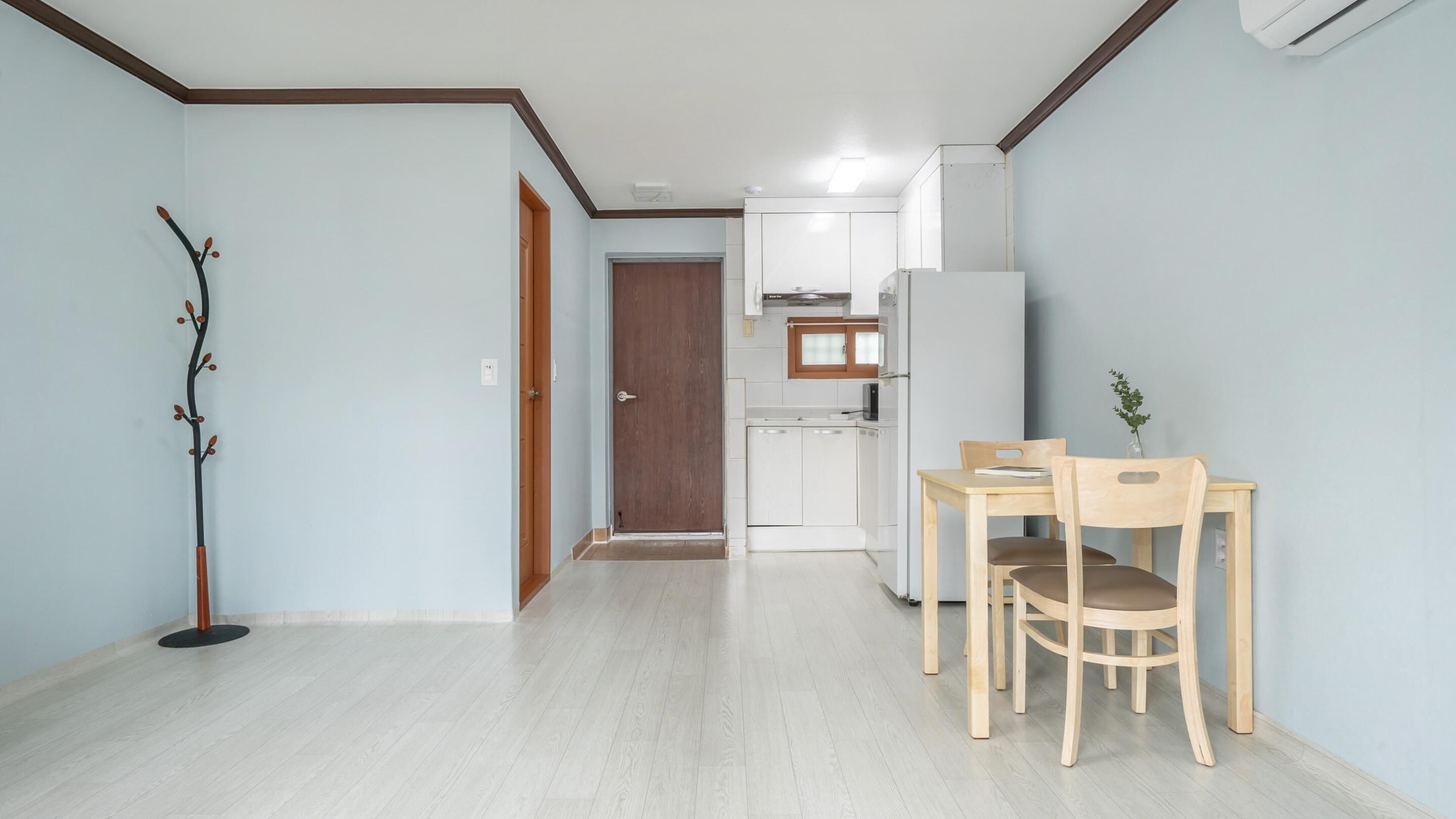 A compact kitchen with white cabinets, a refrigerator, and a dining area with two wooden chairs and a table.